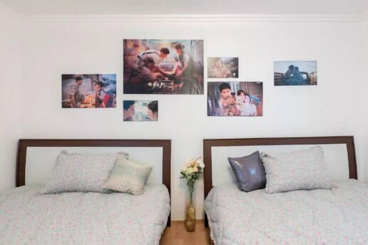 Ein Schlafzimmer mit zwei Betten, einem Wandfernseher und einer kleinen Vase mit Blumen.