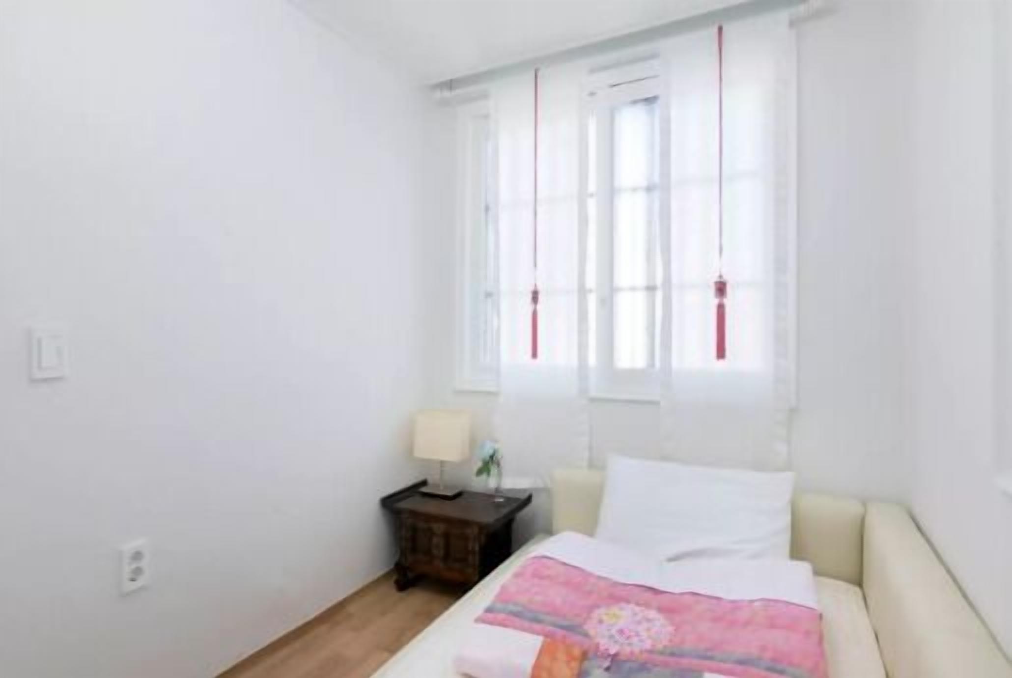 Ein Schlafzimmer mit einem Bett, einem Nachttisch, einer Lampe und einem Fenster mit Vorhängen.