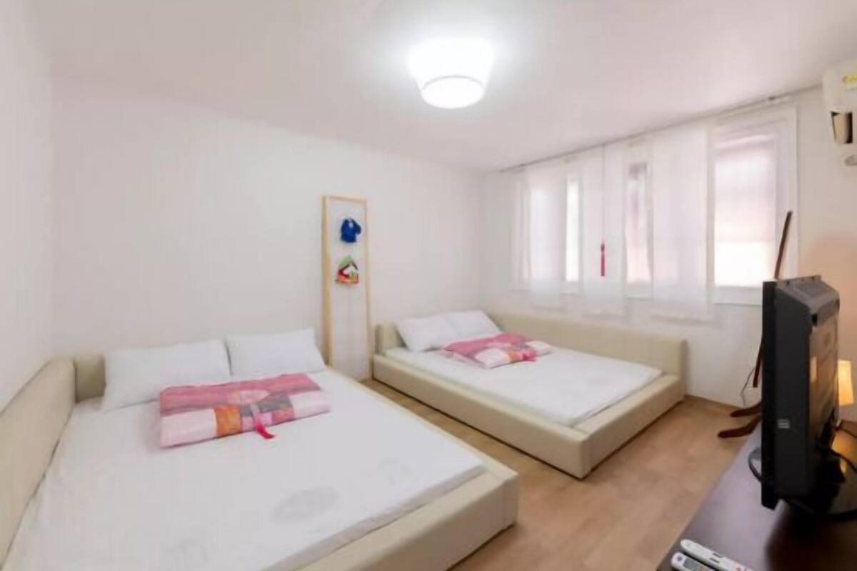 Ein Zimmer mit zwei Betten, einem Fernseher und einem Fenster mit Vorhängen.