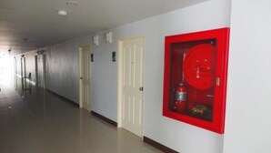 A long, narrow hallway with white walls and doors, a red fire extinguisher mounted on the wall, and a tiled floor. - L Residence Songkhla (Songkhla)