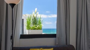 A room with a bed, a window with curtains, a floor lamp, and a potted plant. - Beach View Apartments and Studios (Tel Aviv)