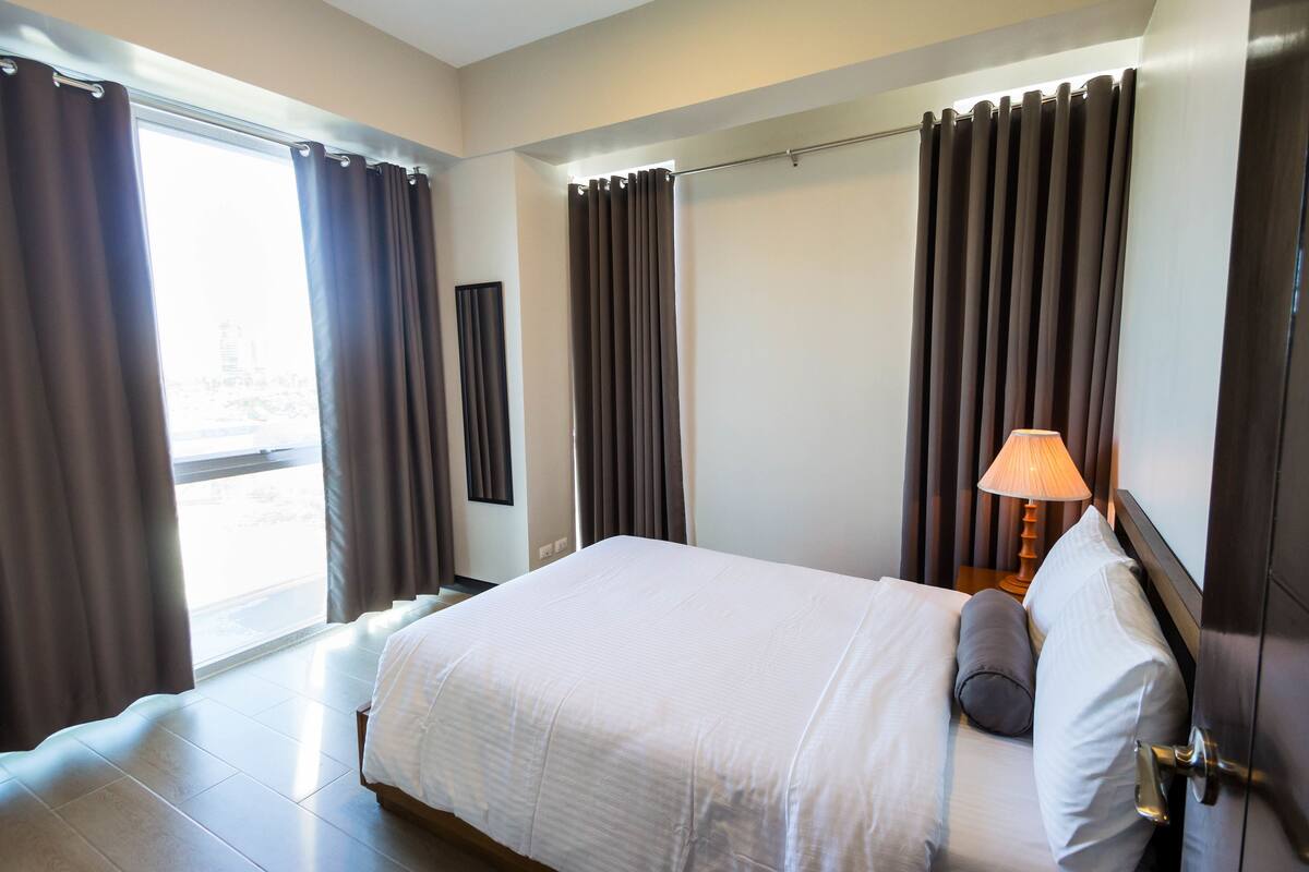 Une chambre d’hôtel avec un grand lit, une table de chevet avec une lampe et une vue sur la ville par la fenêtre.
