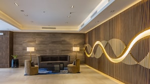 A modern lobby with a sofa, two lamps, a patterned wall, and a wooden floor. - CSuites at 8 Newtown Residences (Lapu-Lapu)