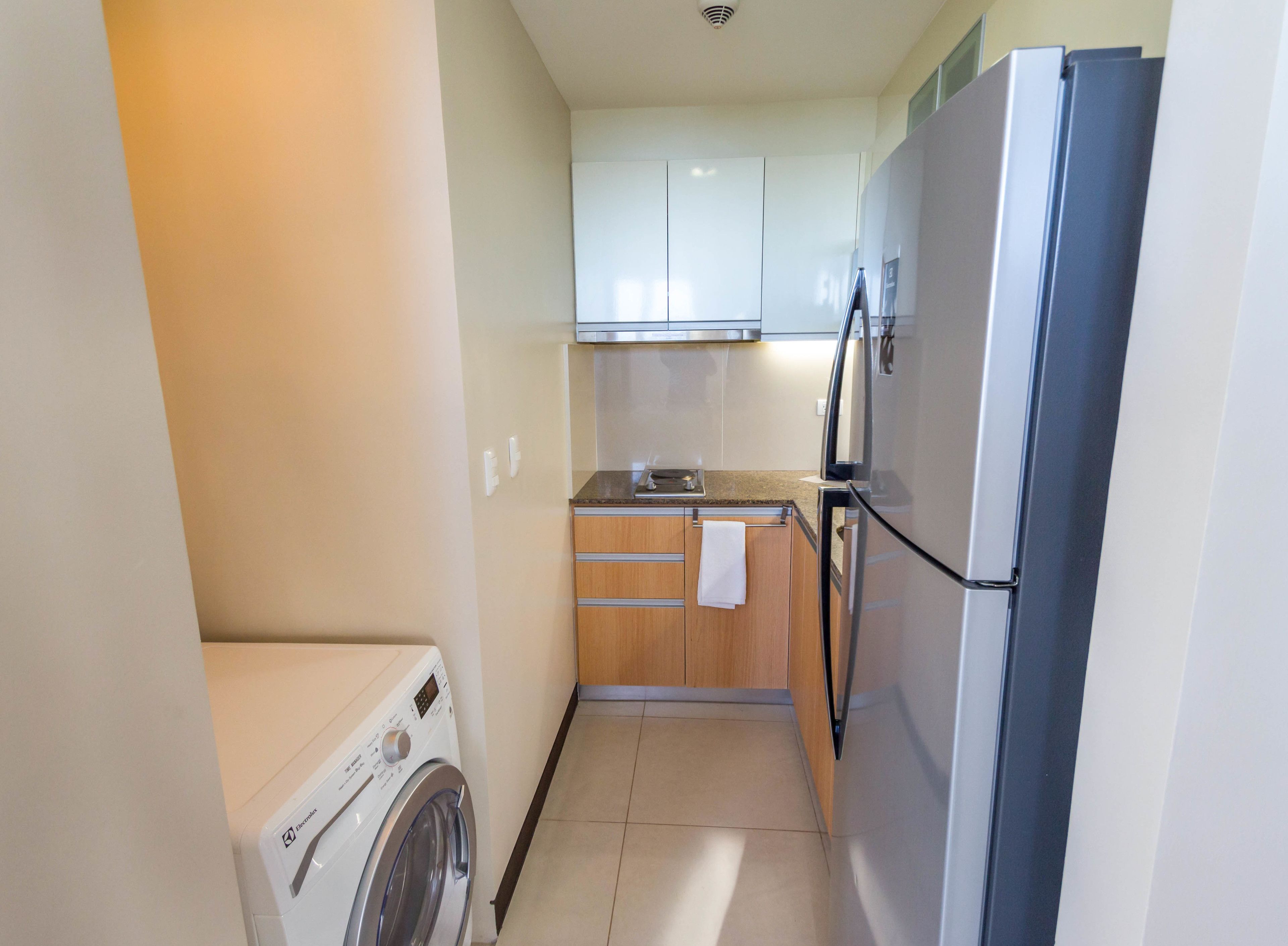 A compact kitchen with a washing machine, a refrigerator, and wooden cabinets.