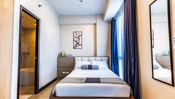 A modern hotel room with a large bed, a bedside table, a nightstand, a mirror, and a shower area.