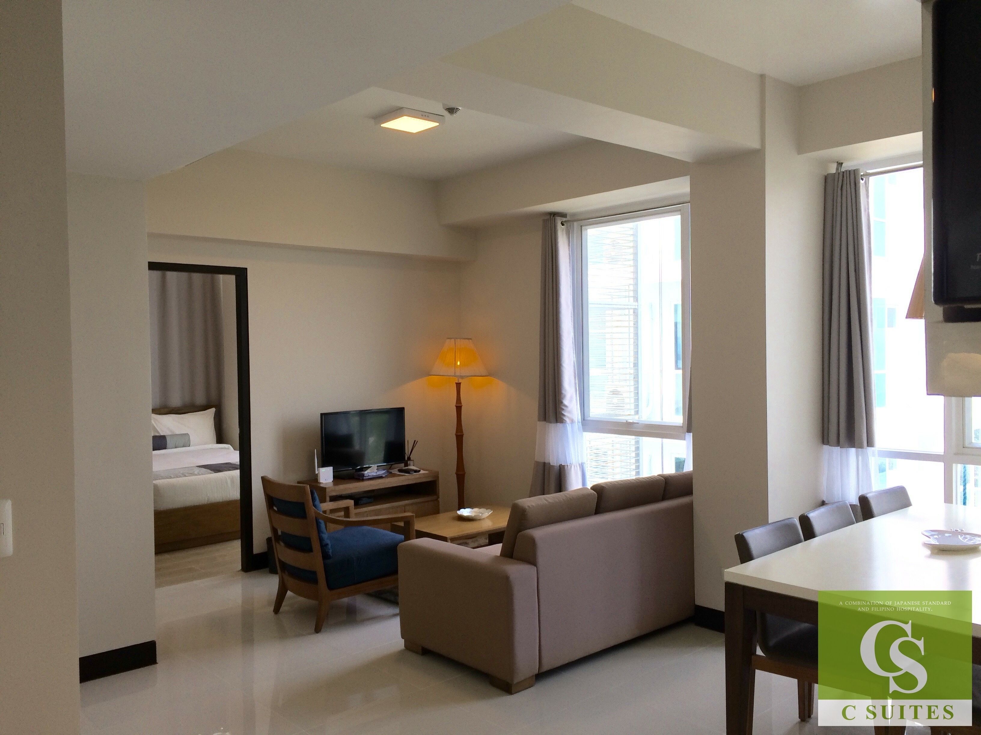 A hotel room with a bed, a TV, a sofa, a desk, and a dining table.