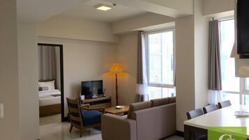 A hotel room with a bed, a TV, a sofa, a desk, and a dining table.