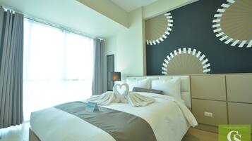 A hotel room with a large bed, a headboard with circular patterns, a bedside table with a lamp, and a window with curtains.