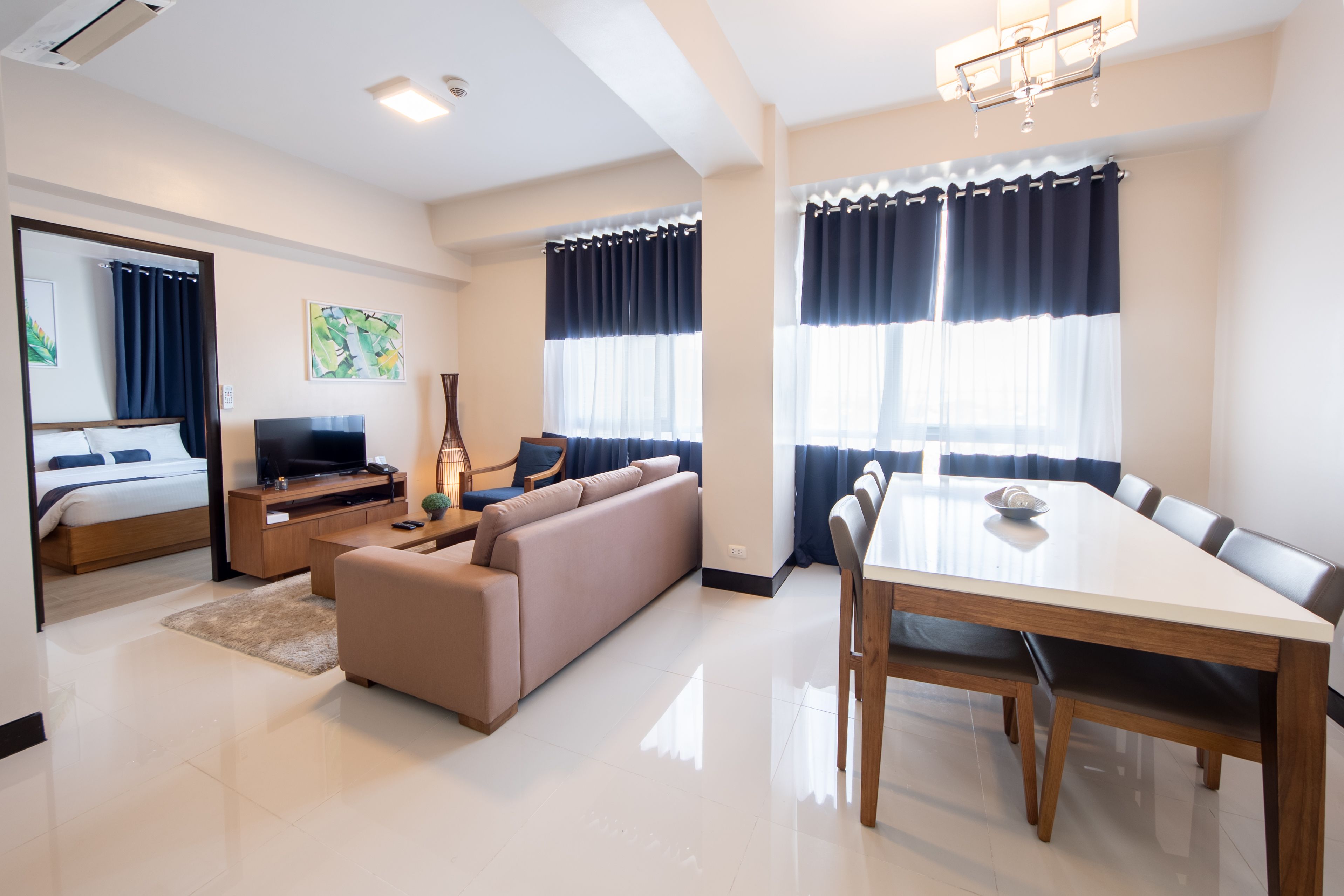 A modern hotel room with a bed, TV, sofa, dining table, and chairs.