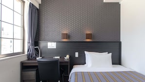 Ein Hotelzimmer mit Bett, Schreibtisch, Stuhl, Telefon und einem Fenster mit Vorhängen.