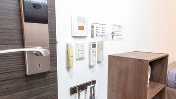 Hotelkamer met een deur, een luchtverkoeler aan de muur, een klein houten plankje en een handdoekhouder.