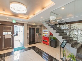 Un moderno vestíbulo de hotel con suelo de mármol, una escalera con un diseño metálico único, una máquina expendedora y un panel digital de ascensor.