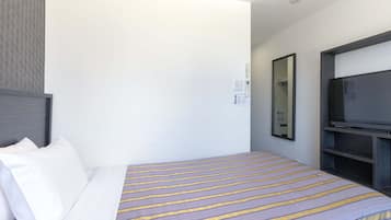 Quarto de hotel com cama, televisão e telefone fixado na parede.