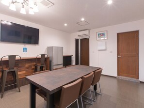 A conference room with a long table, chairs, a flat-screen TV, an air conditioning unit, and a wooden door. - Hotel KOZA (Okinawa)