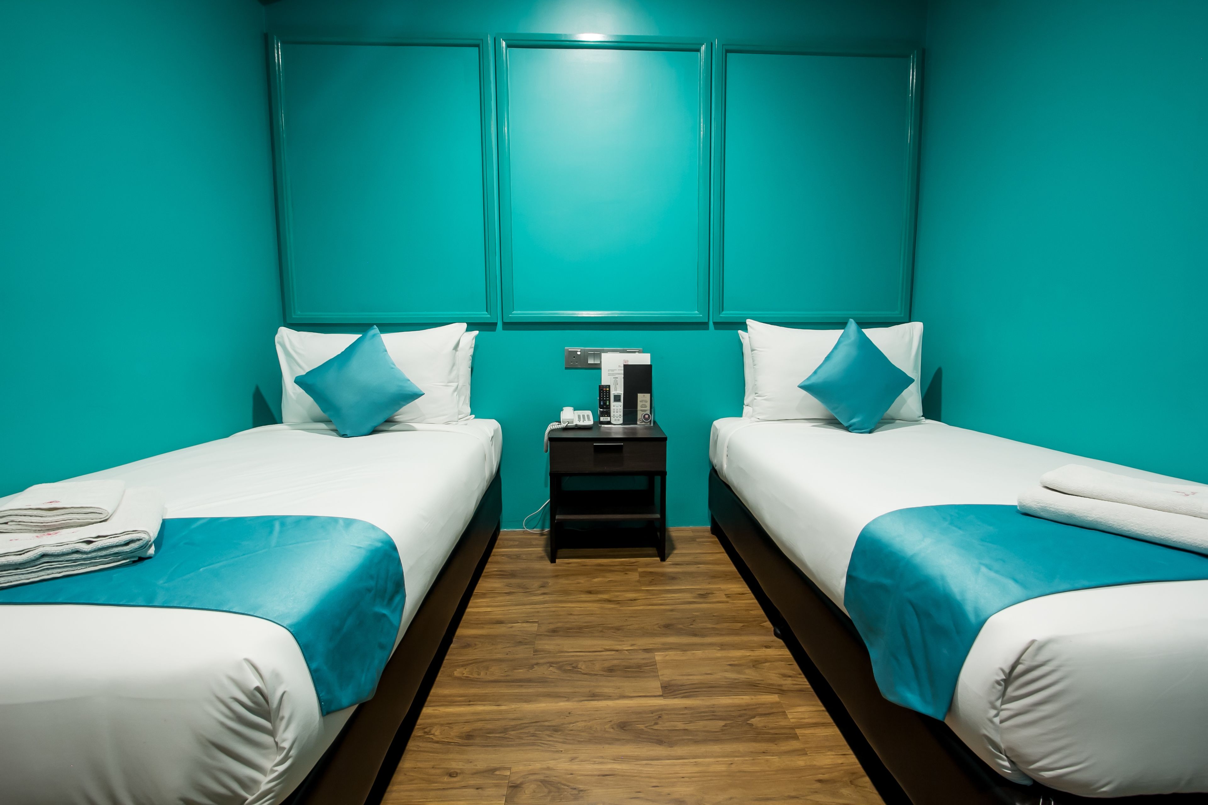 Une chambre d’hôtel avec deux lits, des murs de couleur turquoise, du linge de lit blanc et un plancher en bois.