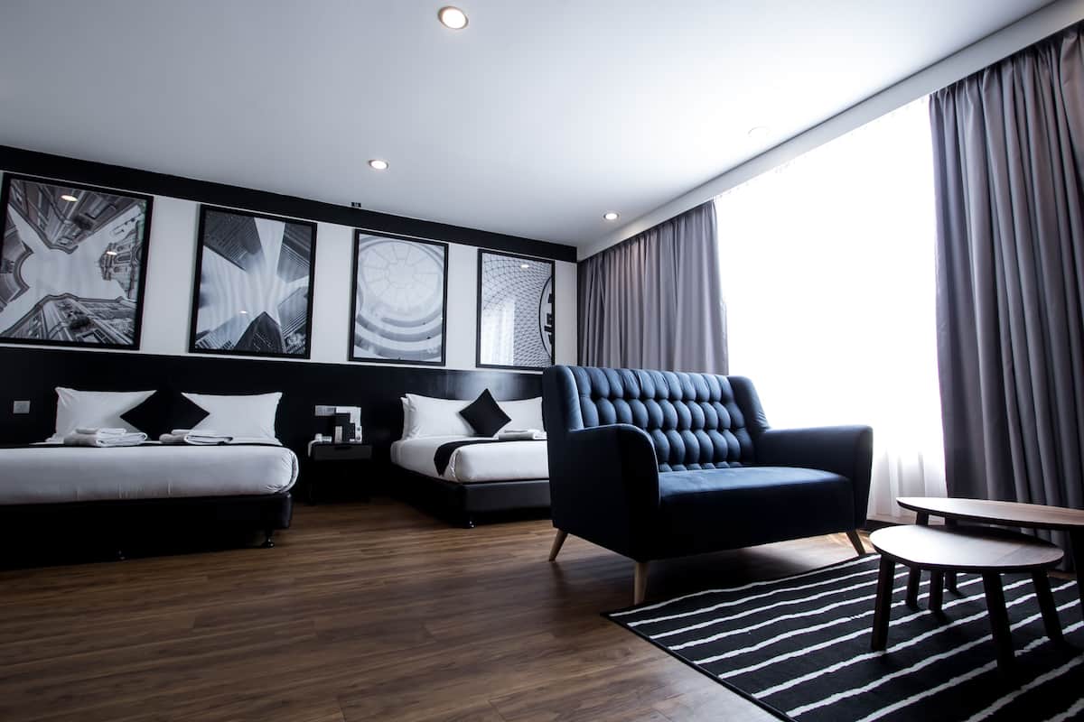 A modern hotel room with a large bed, a sofa, and a small table. There are three large abstract paintings on the wall and a window with curtains.