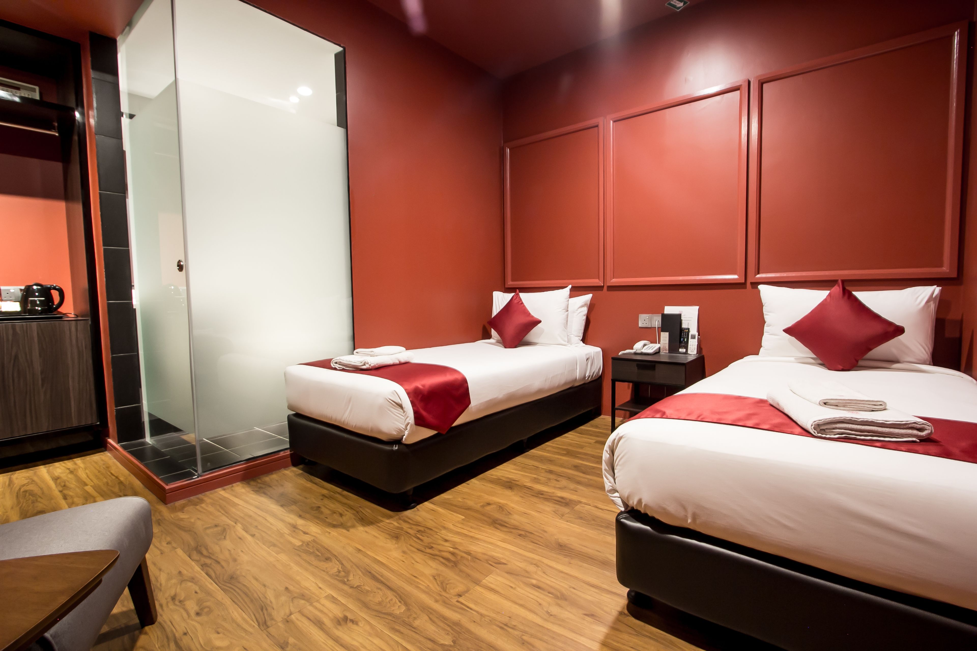 Ein Hotelzimmer mit zwei Betten, Holzboden, Duschkabine aus Glas und einem kleinen Tisch mit Wasserkocher.