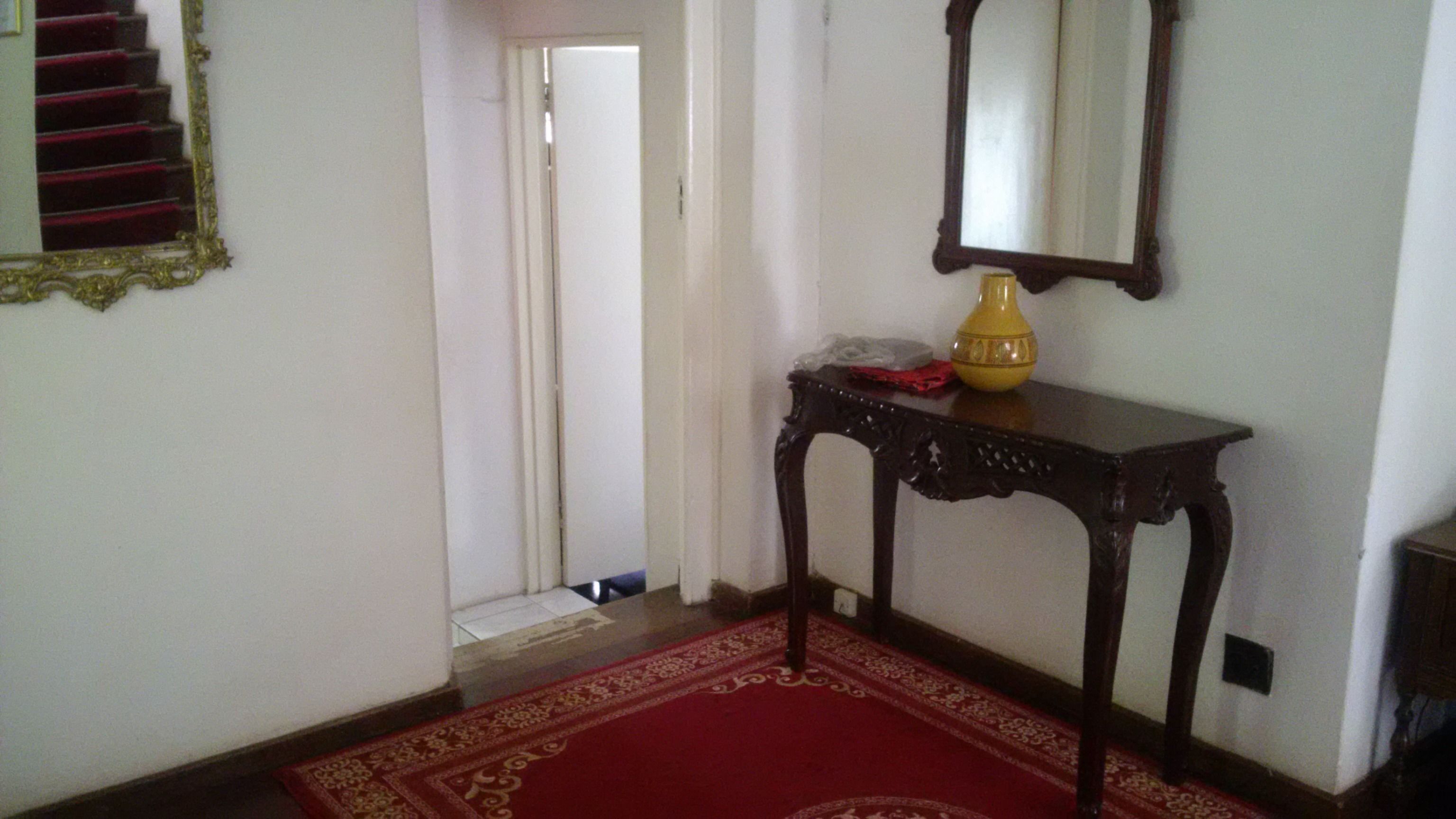 A hallway with a red carpet, a wooden console table with a vase, and a mirror on the wall.