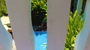 A view through a white fence with a blue pool and green plants in the background. - An Bang Gold Coast Villa (Da Nang)