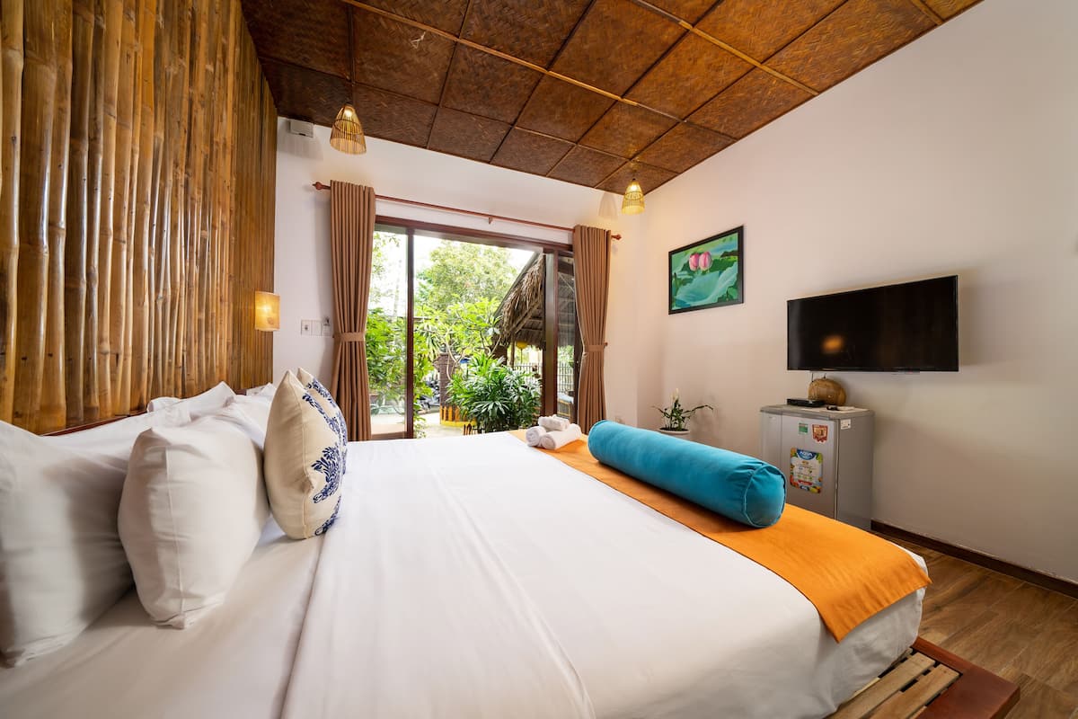 A bedroom with a bed, pillows, a TV, and a small table with a plant.