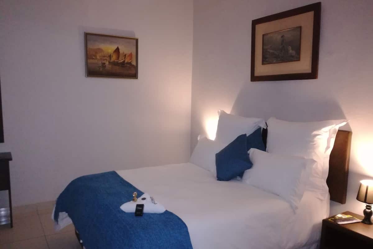 Ein ordentlich bezogenes Bett mit weißer und blauer Bettwäsche, ein gerahmtes Bild darüber und eine Nachttischlampe.