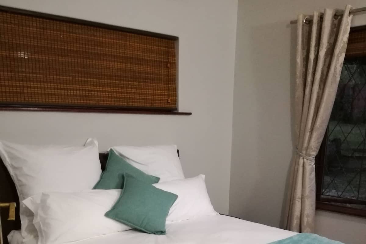 Ein ordentlich bezogenes Bett mit weißer Bettwäsche, einer türkisfarbenen Decke, einem grünen Kissen und einem aufgerollten weißen Handtuch.