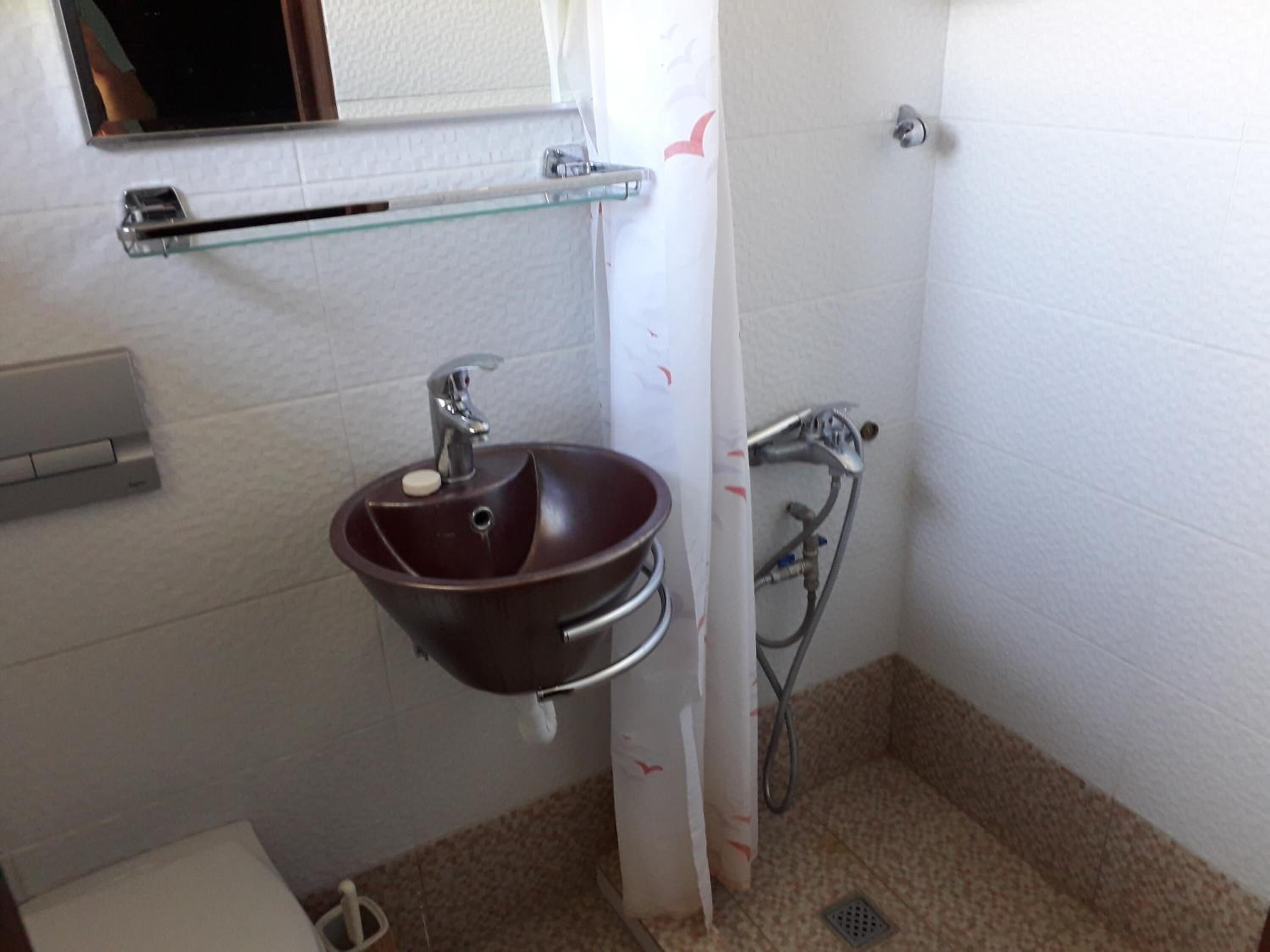 A bathroom with a brown sink, a glass shelf, a shower, and a toilet.