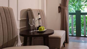 A dining area with two upholstered chairs, a round table, a bottle of wine, two glasses, and a plate with two green apples.