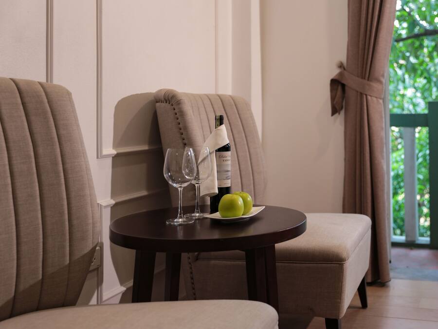 A dining area with two upholstered chairs, a round table, a bottle of wine, two glasses, and a plate with two green apples.