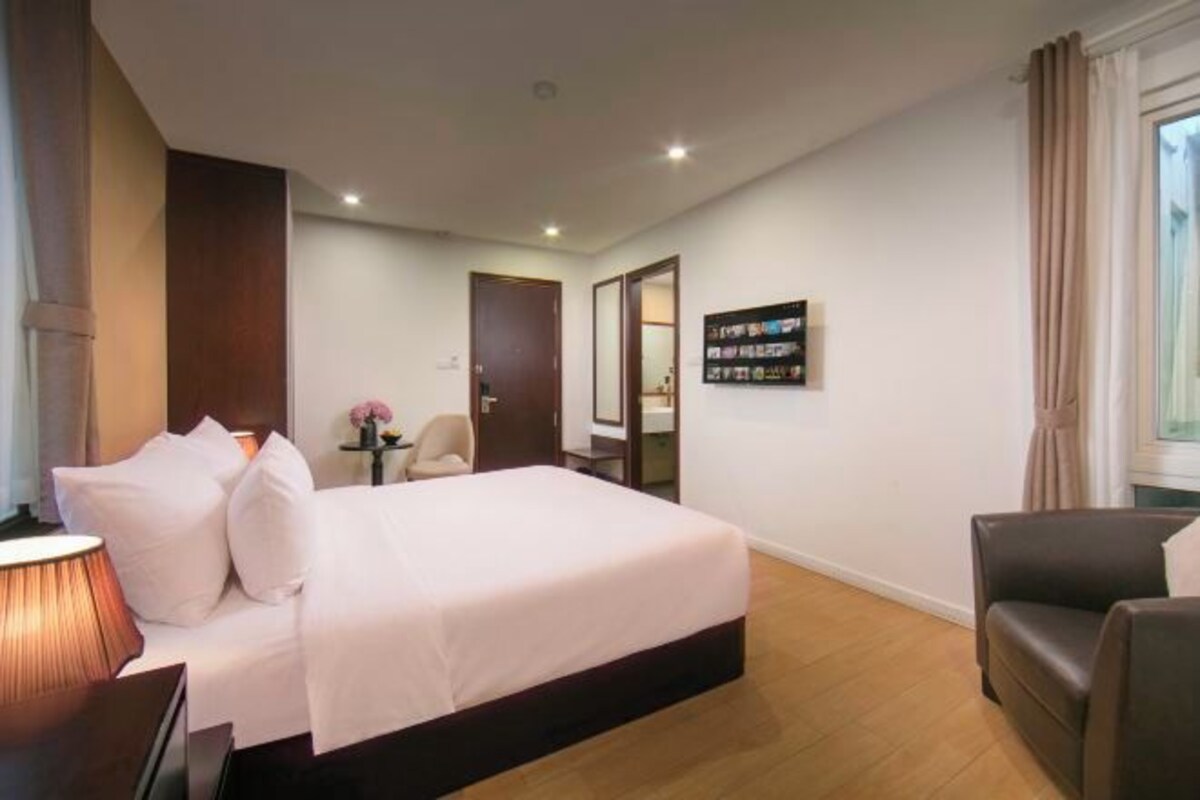A hotel room with a bed, a chair, a desk, and a window with curtains.