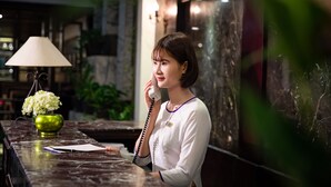 A reception desk with a vase of flowers, a lamp, and a telephone. - Hanoian Central Hotel & Spa (Hanoi)