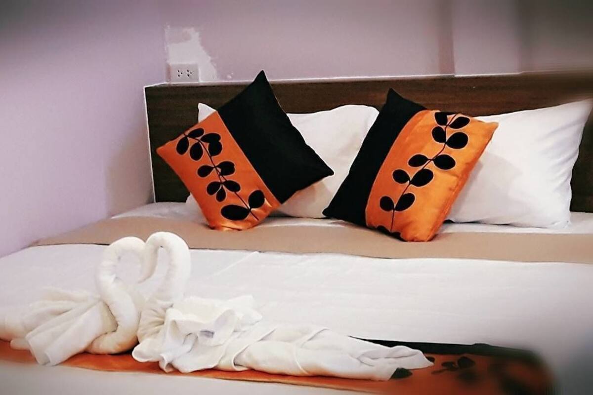 En säng med vita sängkläder och två kuddar med svart- och orangefärgade lövmönster.
