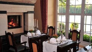 Une salle à manger avec une cheminée, une table dressée pour quatre personnes et une vue sur la verdure à l’extérieur.