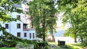 Un bâtiment blanc doté d’une tour circulaire, entouré d’une végétation luxuriante et d’un jardin.
