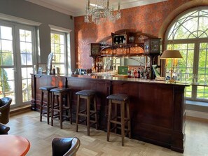 Un espace bar avec un comptoir en bois, des tabourets et un lustre.