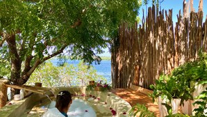 A spa area with a pool, surrounded by greenery and a wooden fence, overlooking a body of water. - Rock and Sea Resort (Watamu)