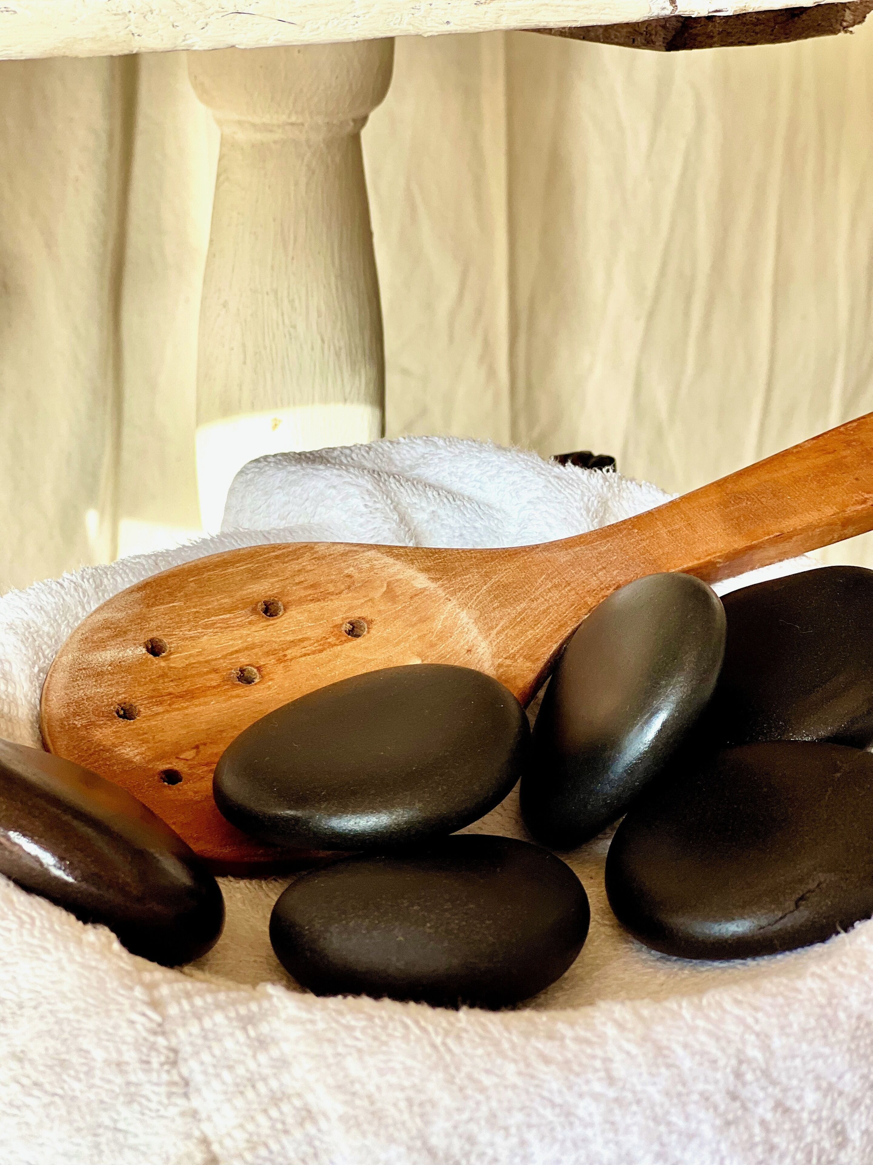 A wooden spoon and black stones on a white towel.