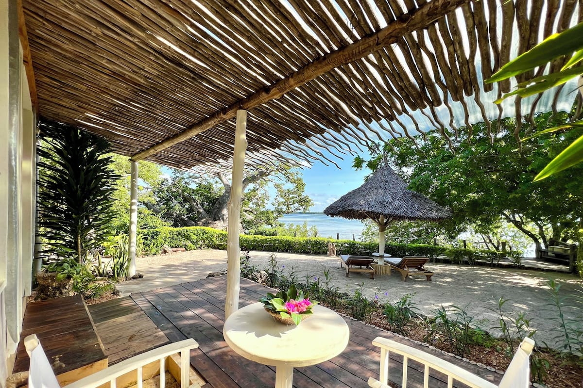Un área de estar al aire libre con mobiliario de madera y una estructura de techo de paja.