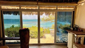 A room with a large sliding glass door leading to a beach view, a wooden bench, a small table with a vase, and a radiator. - Rock and Sea Resort (Watamu)