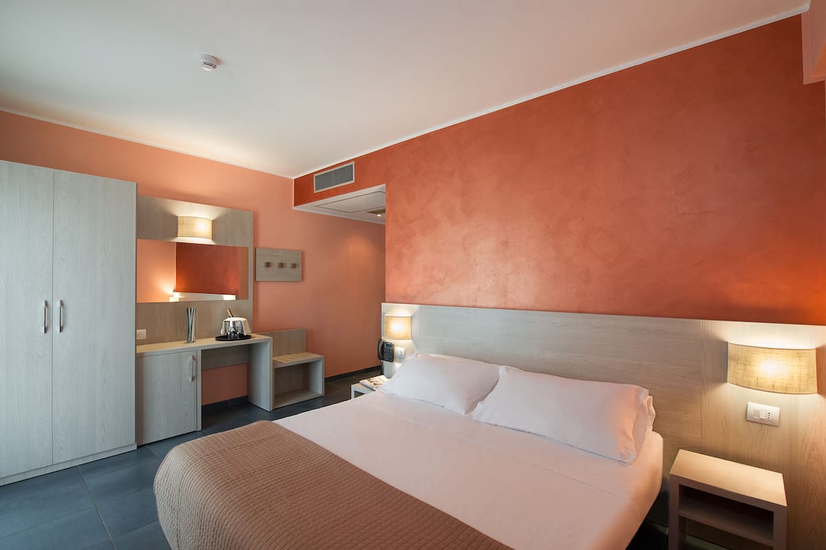 Ein modernes Hotelzimmer mit Bett, Nachttischen, einem Schreibtisch und einem Kleiderschrank.