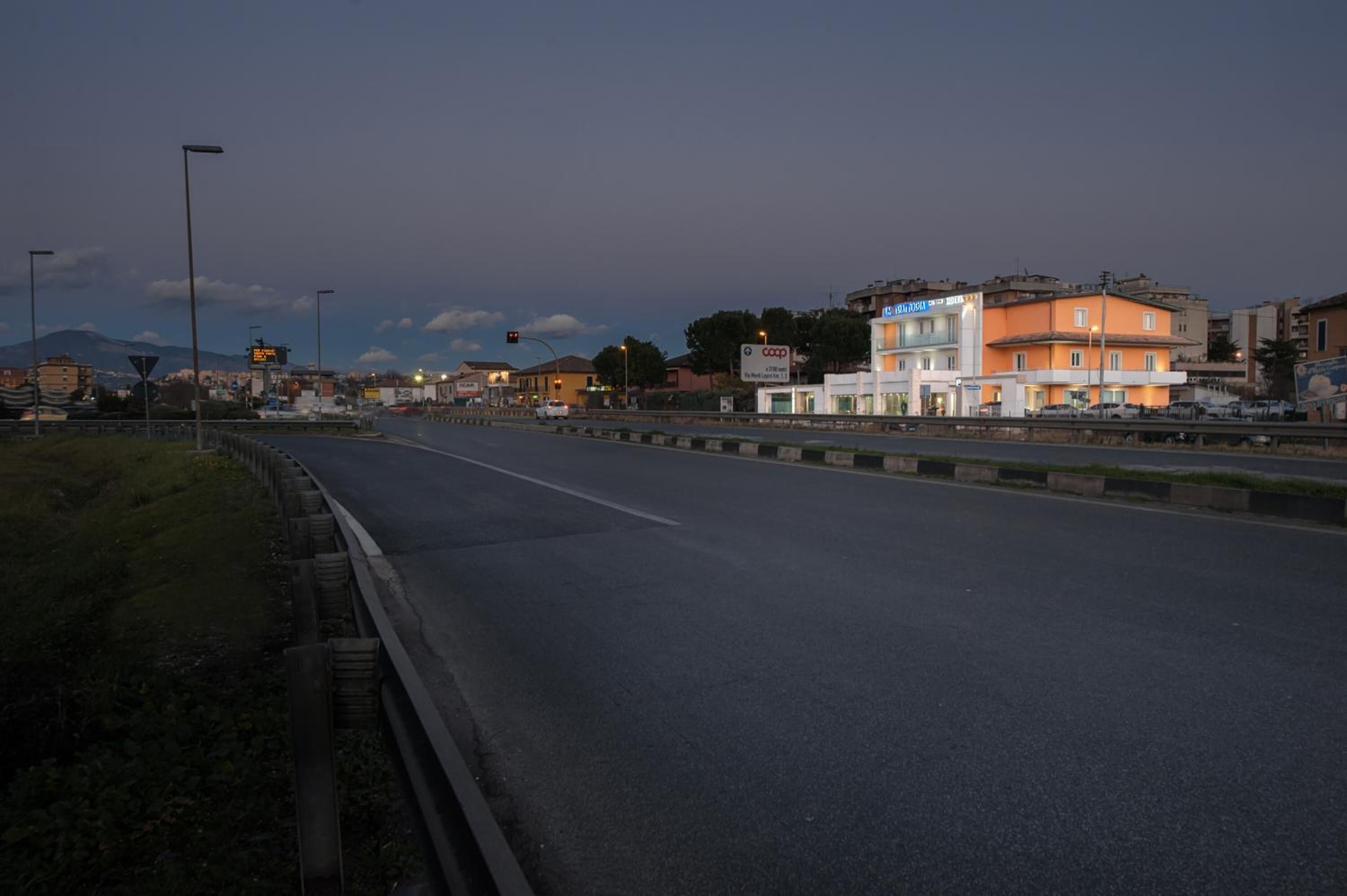 Une route bordée de bâtiments sur le côté droit, dont un immeuble à deux étages avec une enseigne indiquant le mot « coop ».