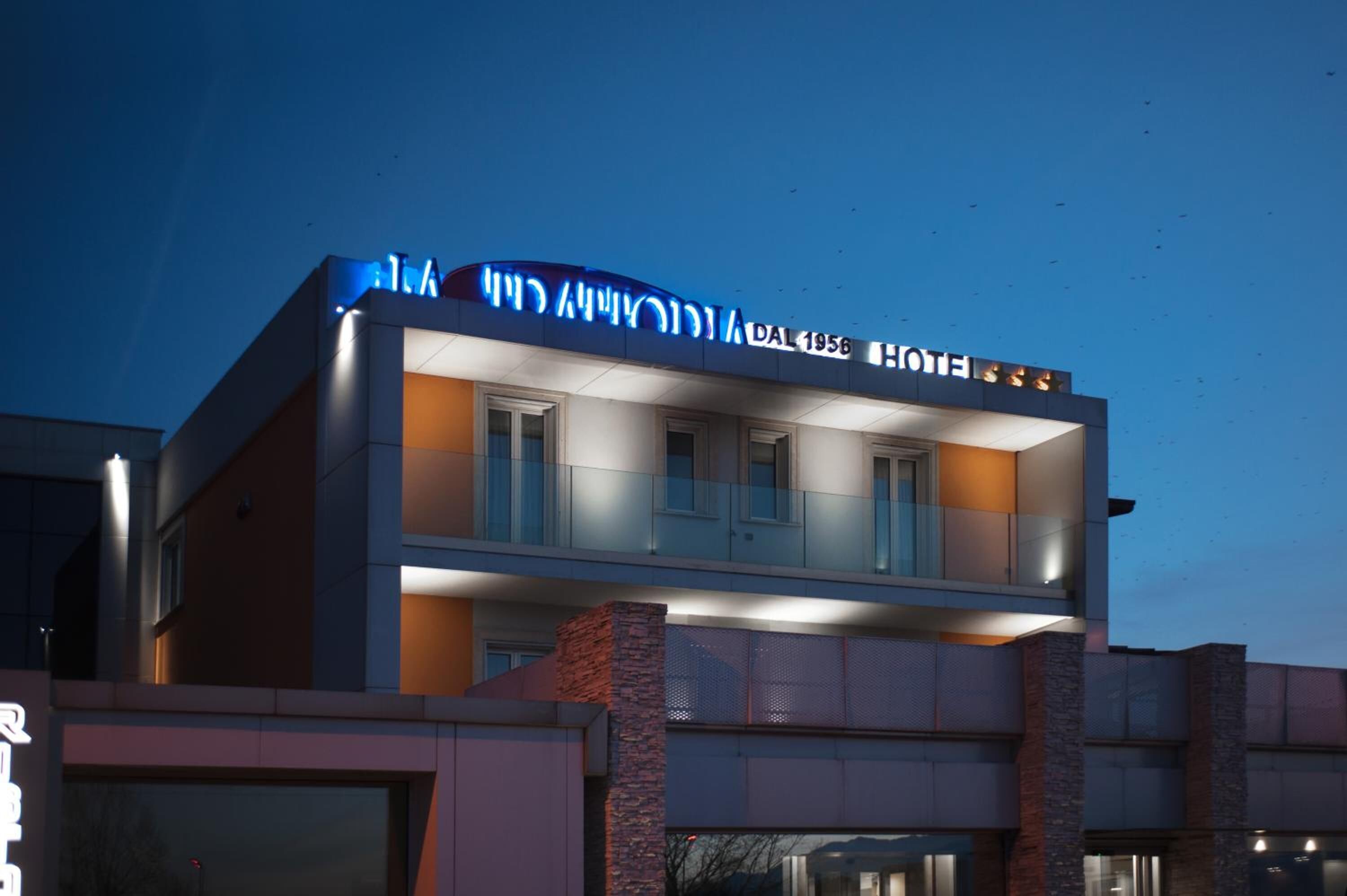 A hotel with a modern facade, a balcony on the second floor, and a sign indicating the year 1956.