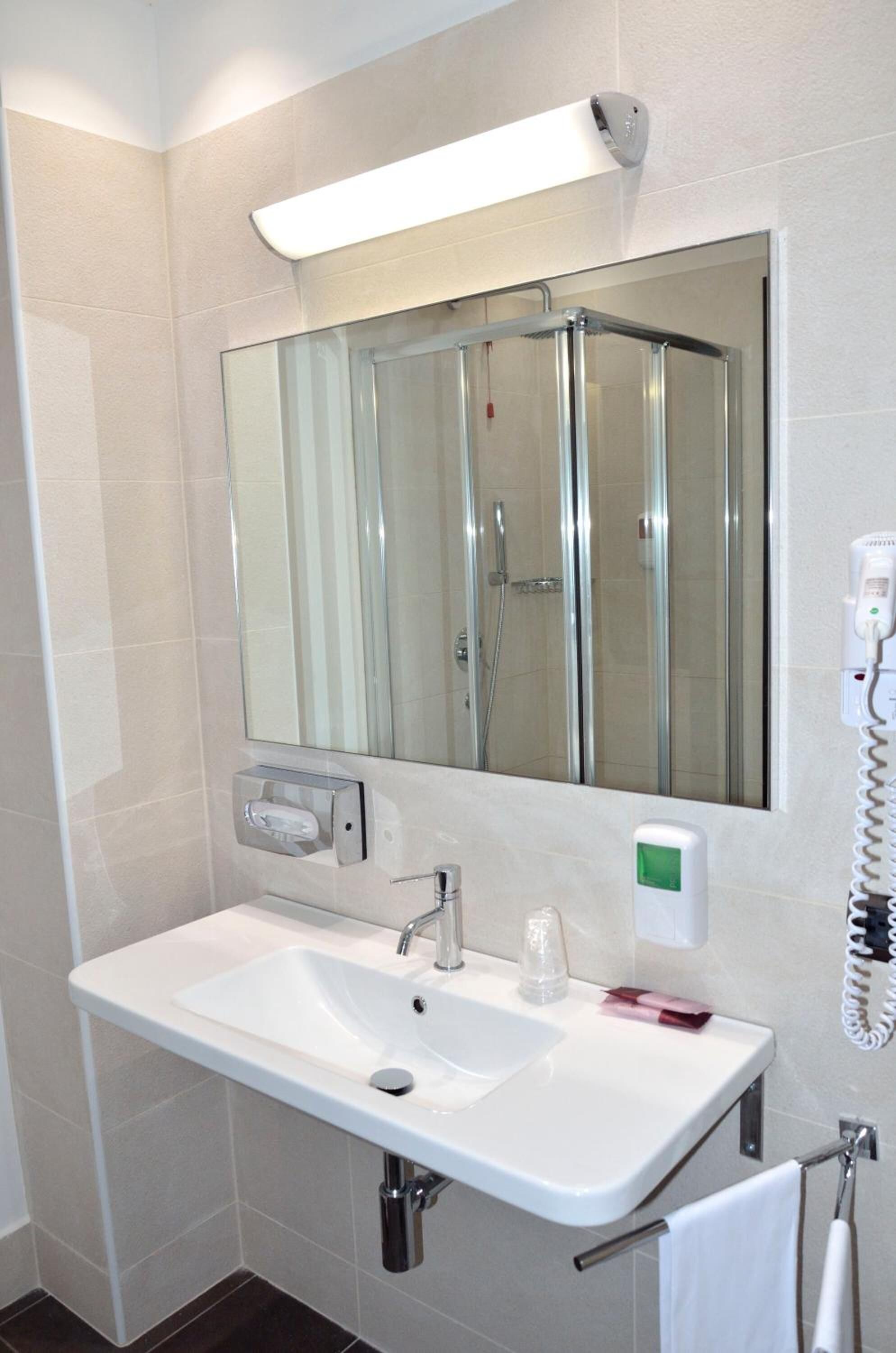 A modern bathroom with a white sink, a large mirror, a glass shower enclosure, and a towel rack.