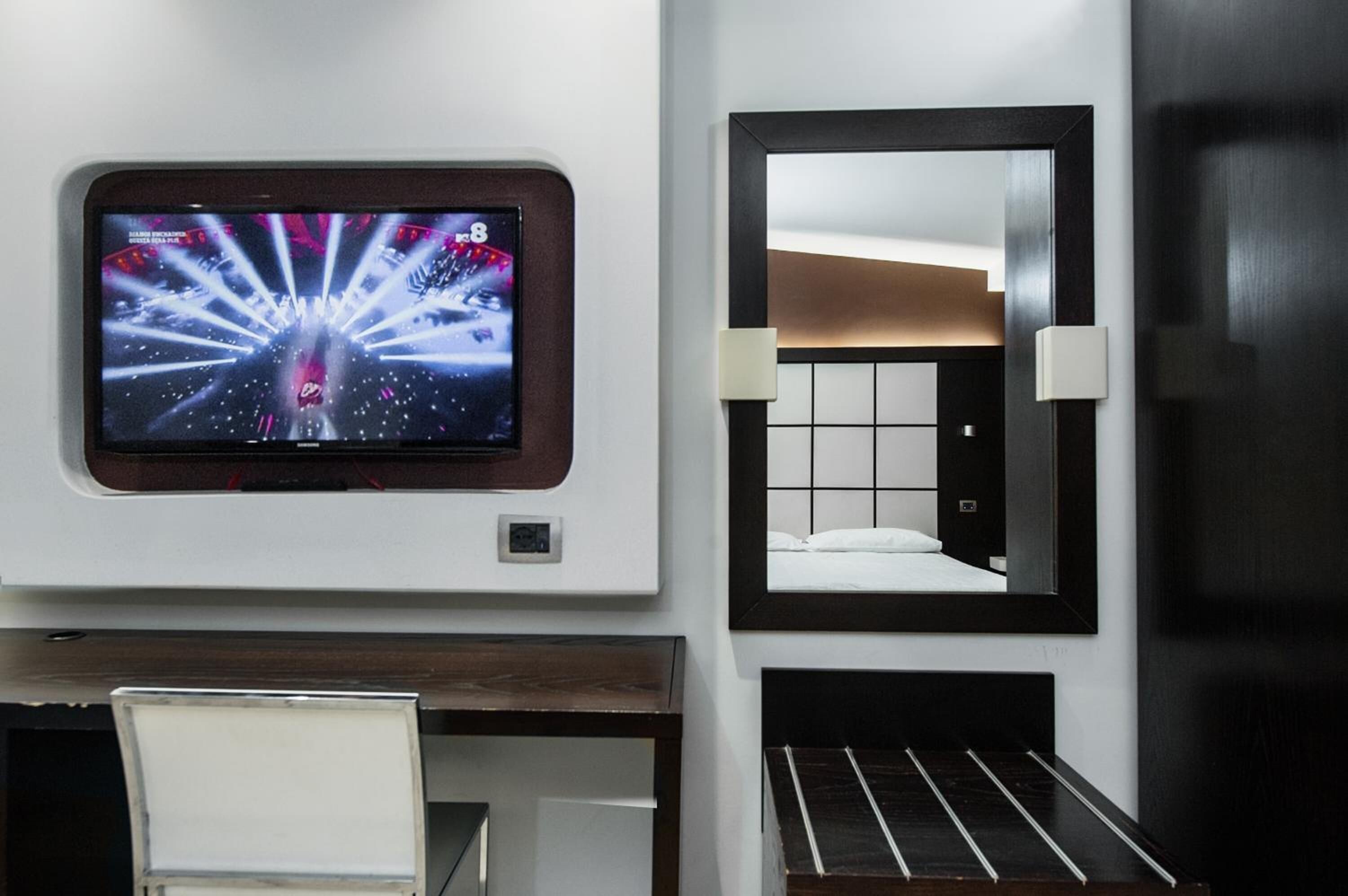 Habitación de hotel con televisión montada en la pared, una cama con cabecero y un espejo sobre la cama.