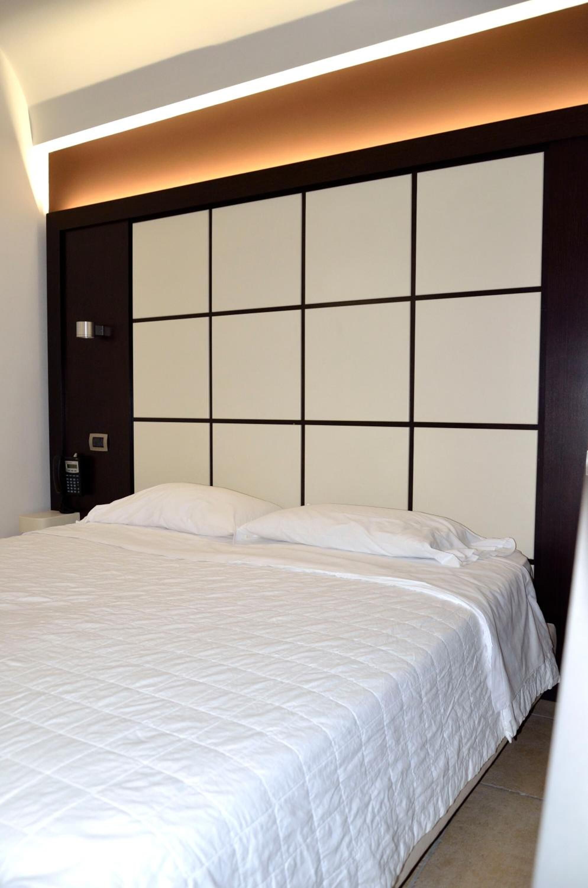 Quarto de hotel com uma cama grande, cabeceira com padrão quadriculado, telefone ao lado da cama e luminária fixada na parede.