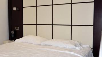 Habitación de hotel con una cama grande, cabecero con diseño de cuadrícula, teléfono en la mesita de noche y lámpara de pared.