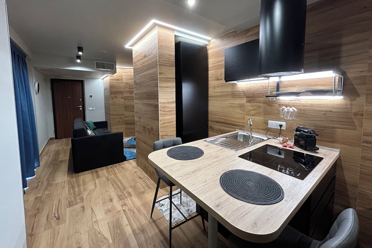A modern kitchen with a central island, built-in appliances, and a black range hood.