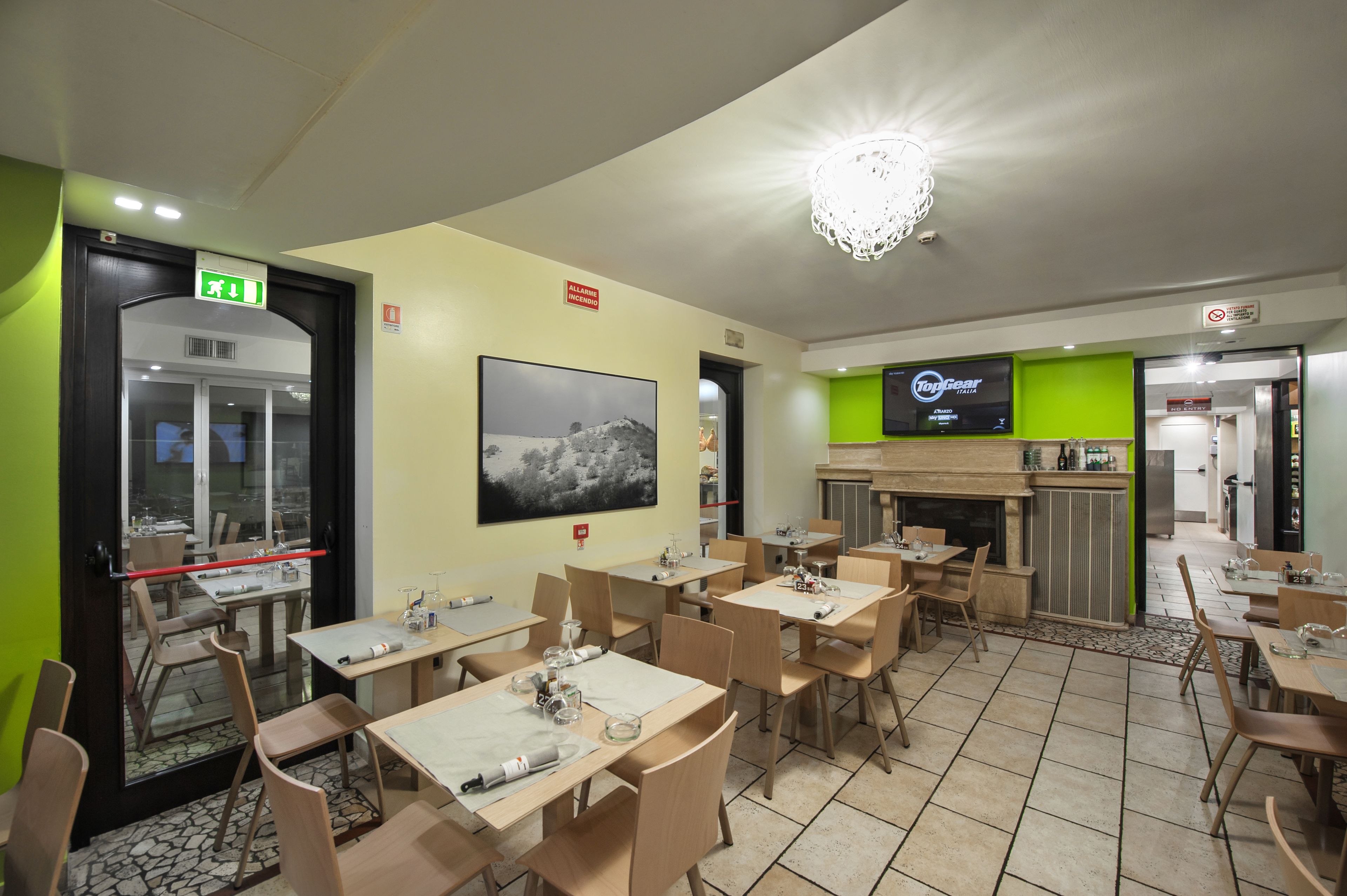 A restaurant with multiple tables and chairs, a fireplace, and a television screen displaying a menu.