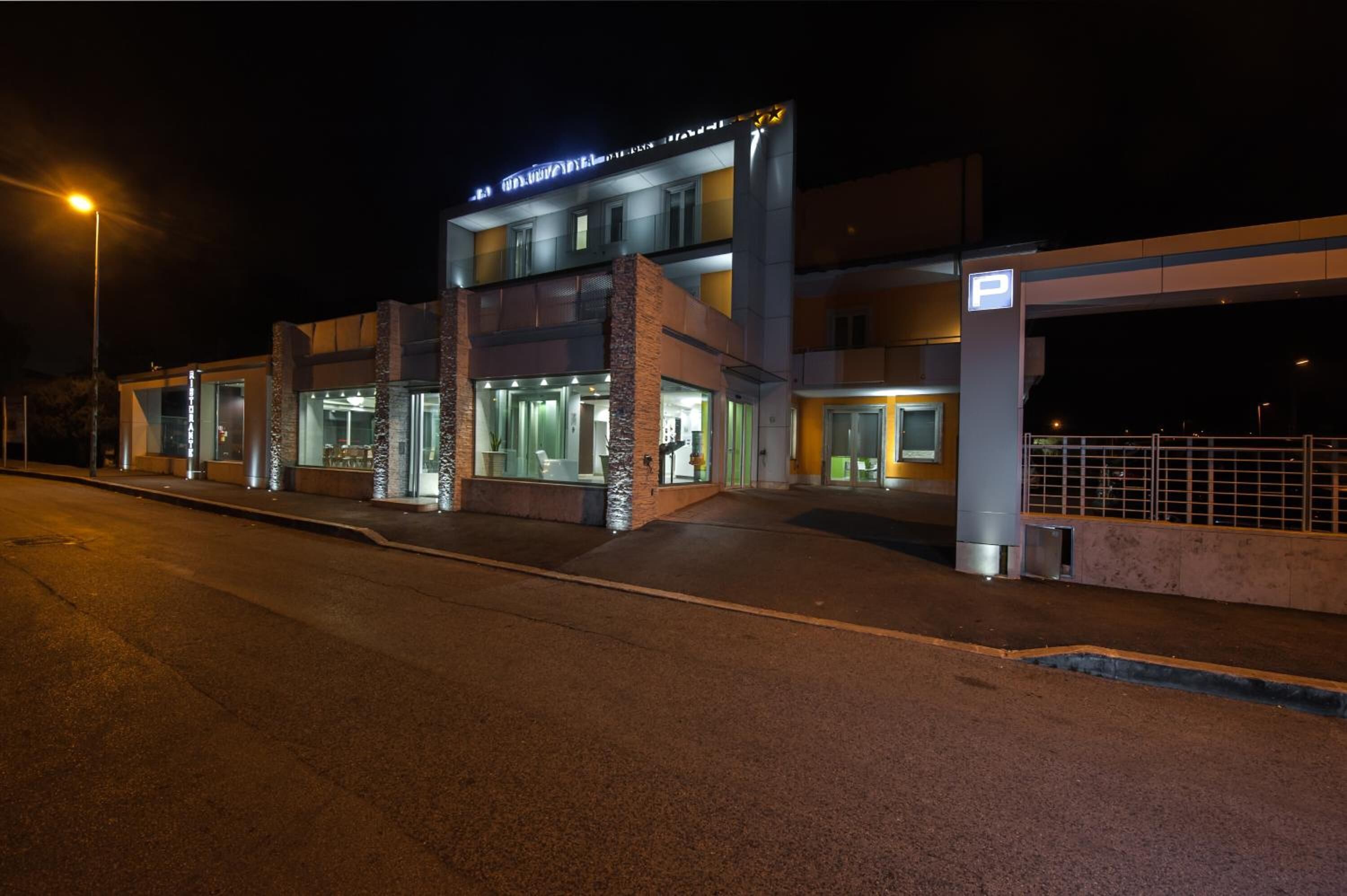 A modern hotel with a glass facade, a parking area, and a sign indicating the hotel's name.