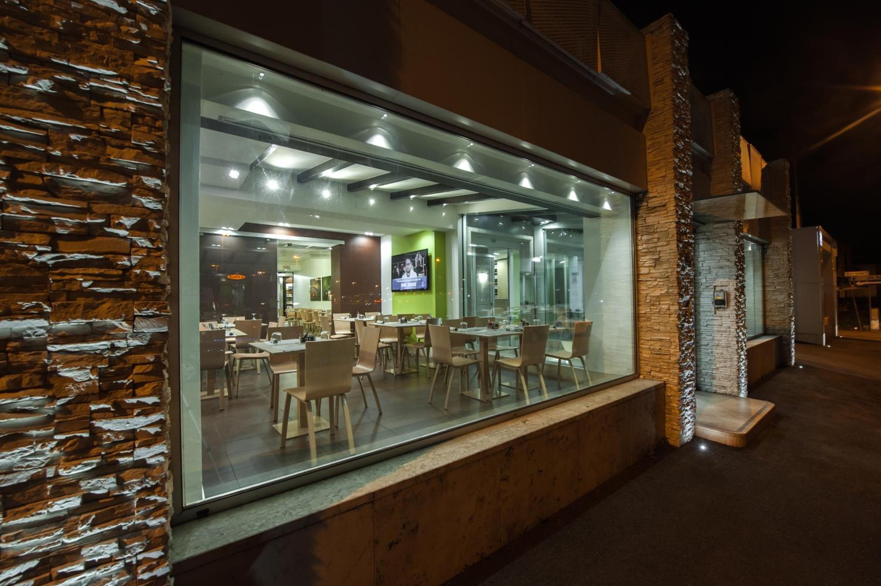 A modern restaurant with a glass facade, stone accents, and a green accent wall.
